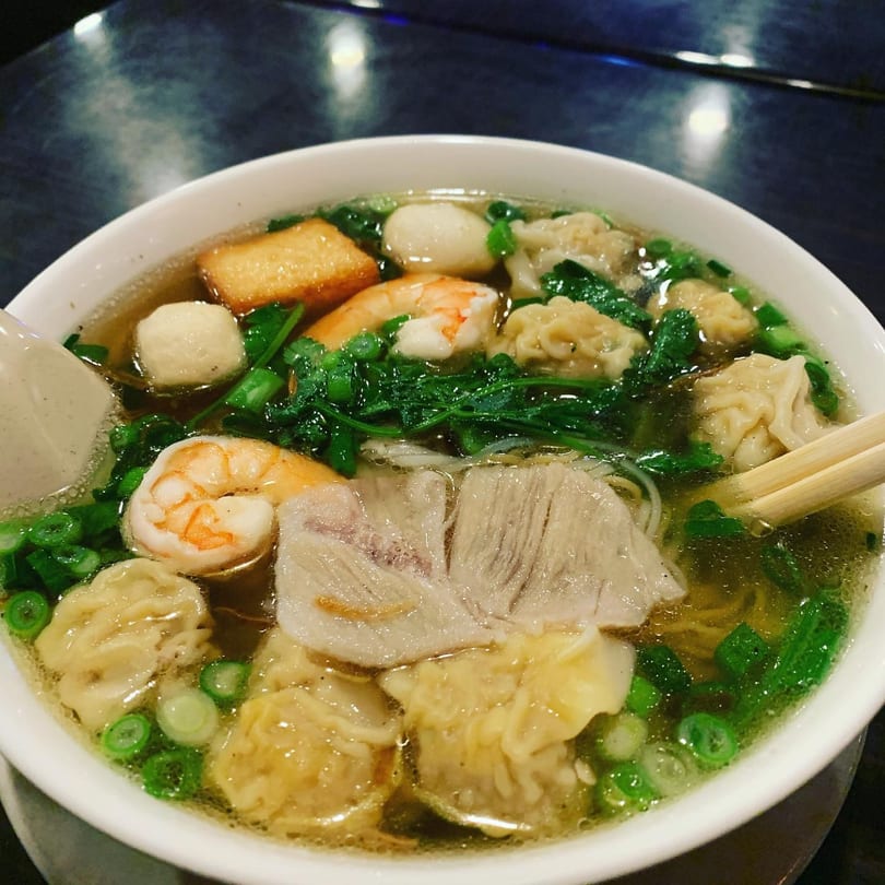 A bowl of Vietnamese noodle soup with shrimp, pork, wontons, fish balls, and greens.