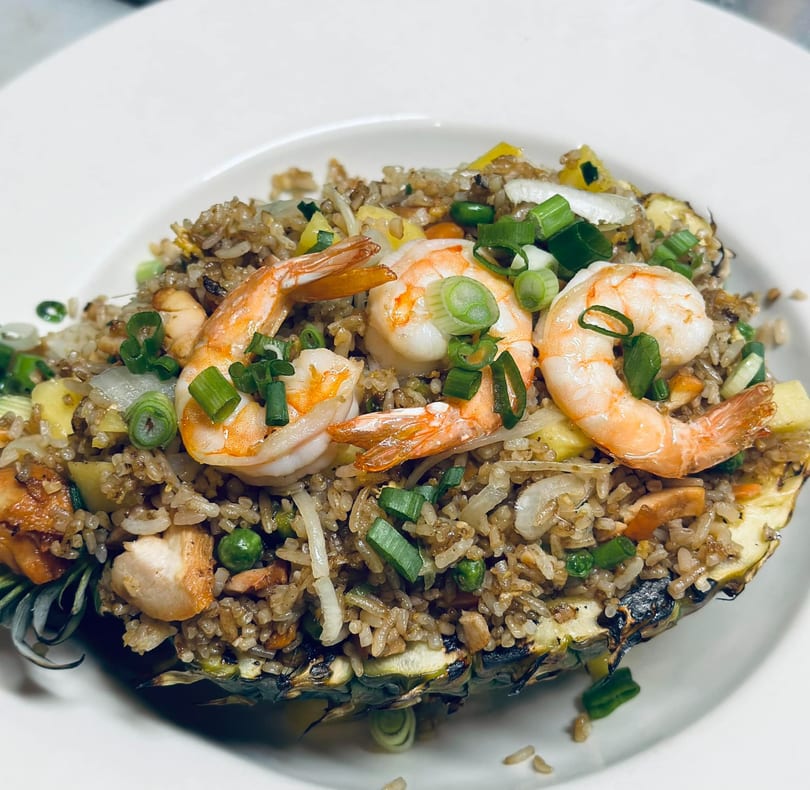 Shrimp and chicken fried rice served in a carved pineapple half, garnished with green onions.